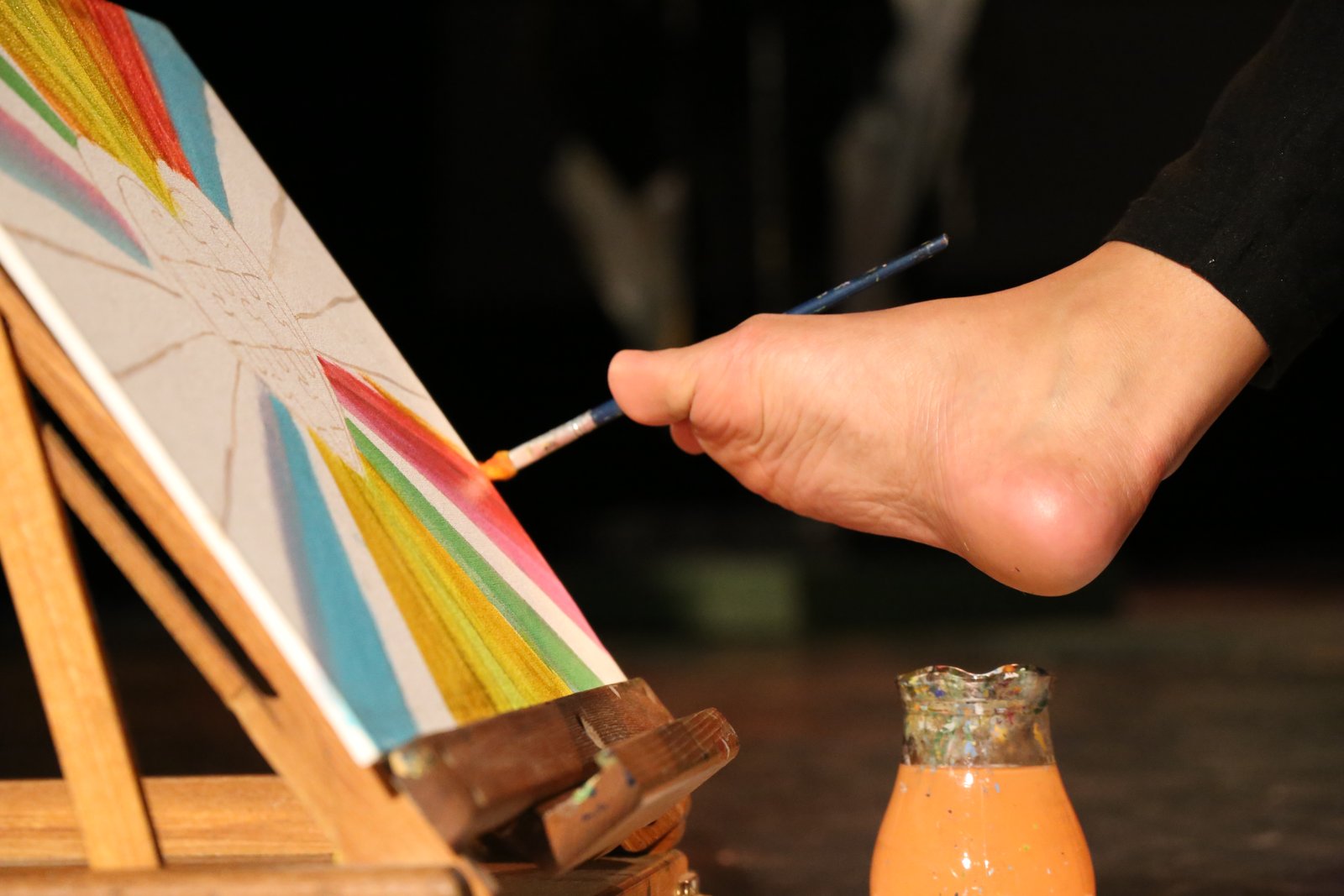 Primer plano del pie de Antonela pintando rayos de colores sobre un lienzo durante una demostración