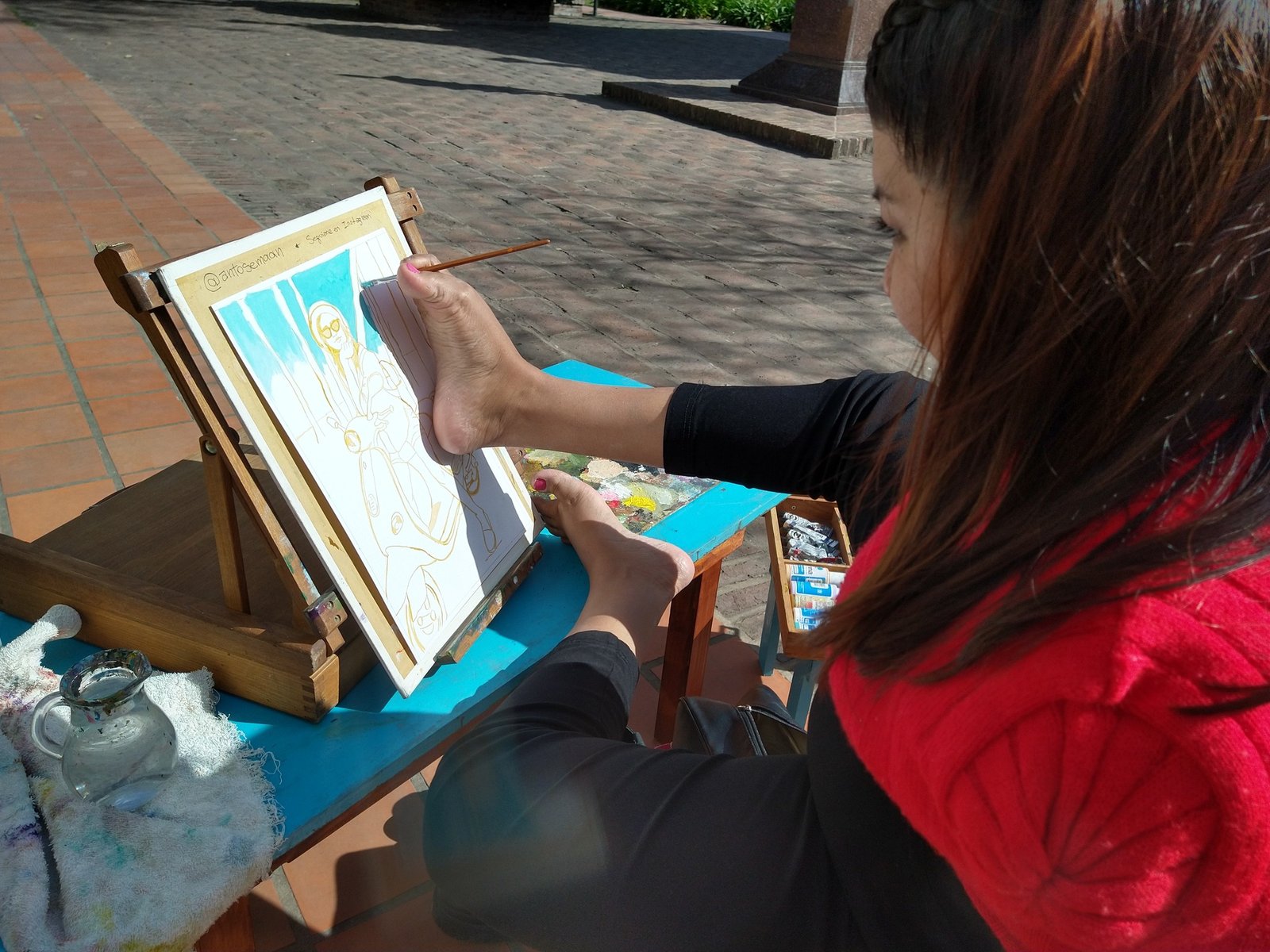 Antonela pintando al aire libre en una plaza, frente a su caballete